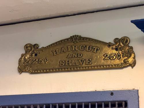 Vintage brass 'Haircut and Shave 25 cents' sign at Balcony Barber Shop